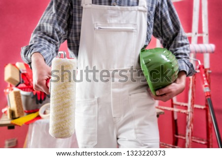 Young Caucasian house painter worker in white work overalls, holds the roller with your hands. Construction industry. Work safety. 