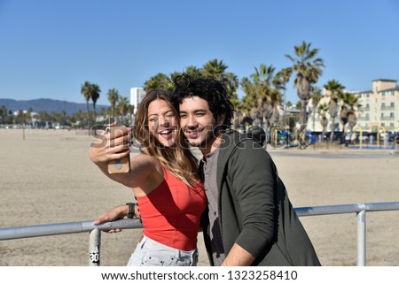 Young couple taking cell phone photos of themselves on the beach in a tropical resort town