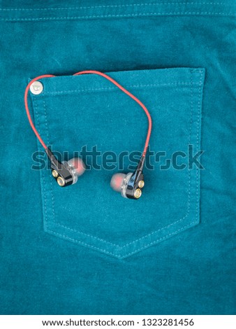 Headphones with red wire sticking out of the pocket of green jeans.