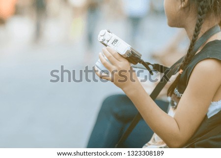 Asian girl learning to use a mirrorless camera with her mom in the public park. Selective focus on hand.