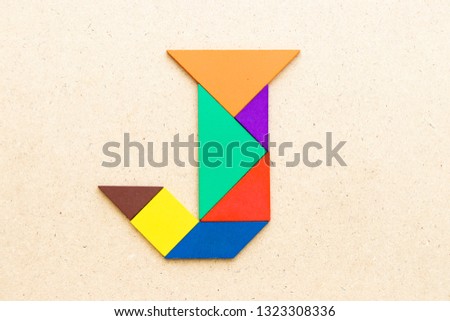 Tangram puzzle in alphabet letter J shape on wood background