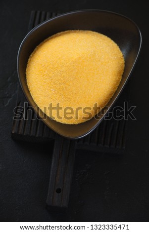 Bowl of uncooked polenta over black stone background, vertical shot, selective focus