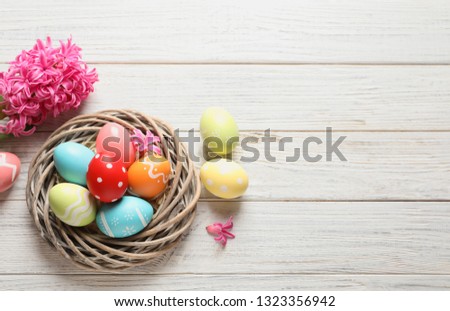Flat lay composition of wicker nest with colorful painted Easter eggs and flower on table, space for text