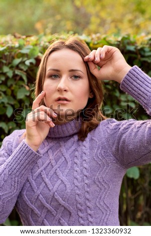 Portrait of a natural blue-eyed woman model in a purple sweater in the autumn city park.