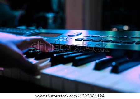 Person playing a piano keyboard in concert with spotlights, close-up of hand