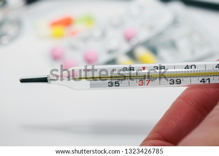 medical glass thermometer with high temperature in hands on the background of various drugs, vitamins, antibiotics and tablets