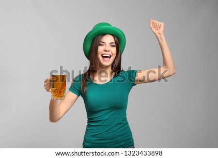 Beautiful young woman in green hat and with mug of beer on grey background. St. Patrick's Day celebration