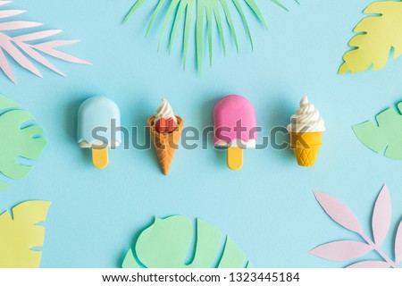 Summer background made of ice cream miniatures and colorful paper tropical leaves minimal creative concept.