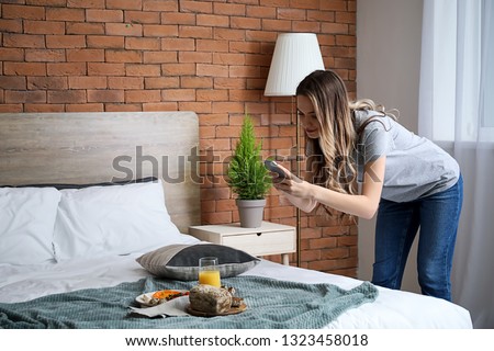 Female food photographer with mobile phone taking picture of tasty breakfast at home