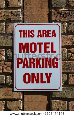 This area motel parking only sign, bold red text on white, brick background. Portrait orientation.