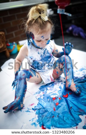 An adorable little toddler, girl has fun playing with colouring paints, getting covered in paint having lots of fun, shot on a white background, and in a home setting, family portrait fun,