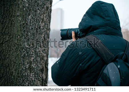 A man in a jacket with a hood and a briefcase on his back, holding a camera and taking pictures of a tree, a man doing a macro photo of the bark of a tree