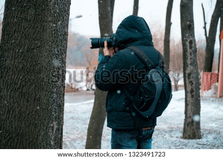 A man in a jacket with a hood and a briefcase on his back, holding a camera and taking pictures of a tree, a man doing a macro photo of the bark of a tree