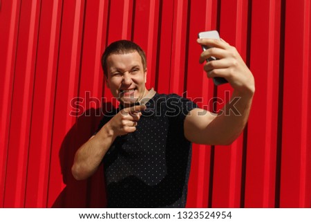 Handsome adult man using his cellphone, smiling on red background with free space. Image of happy young man standing over red wall background making selfie photo on mobile phone