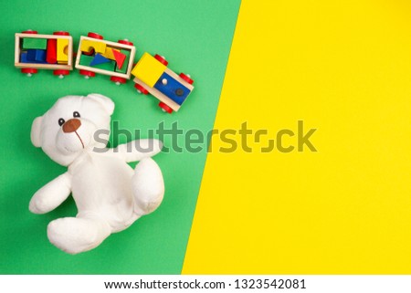 Baby kids toys background. White teddy bear and wooden toy train on multicolored yellow and green background