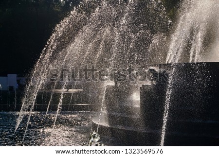 water jets of a large fountain shine in the rays in the central city park of the city in the air on a sunny summer day