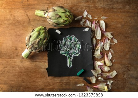 Tasty raw artichokes with picture on wooden table