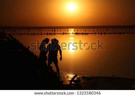 On a salt lake in the setting sun, family, father with a hat, mother and small child on the horizon with a silhouette walk along the shore