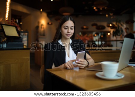 Young prosperous business woman online searching information on account via mobile phone while sitting in luxury restaurant during work break. Female jurist using cell telephone for chat in internet 