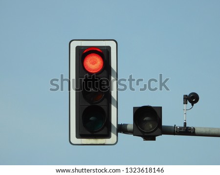 Closeup view of red traffic lights with camera tracking and controlling the flow of cars mounted on a grey metallic pole above the road, Berlin, Germany. Clear bright blue sky in the background