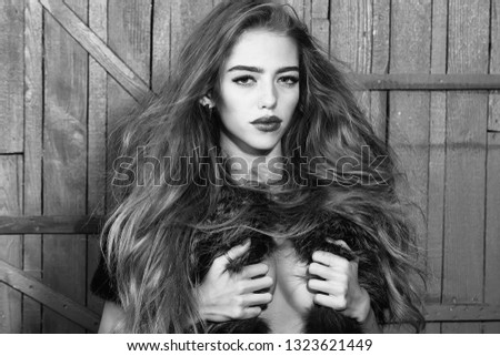 One funny young fashionable woman with beautiful long curly hair in waist coat of blue fur standing in hairdressing saloon in studio on wooden background, horizontal picture