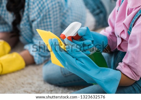 cropped view of african american child spraying cleaning liquid on yellow rubber rag