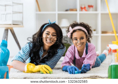 smiling african american woman and daughter in bright rubber gloves lying on carpet 
