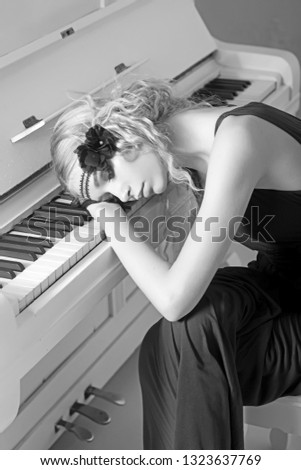 Beautiful blond girl in headband lying on keyboard of white piano with her eyes closed. Back to 1920s.