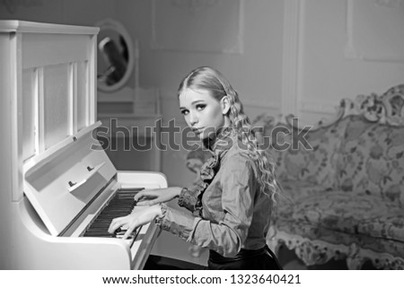 Young Victorian lady in a tender blue dress playing piano. Lovely blond woman sitting in room with vintage furniture. Home education concept.
