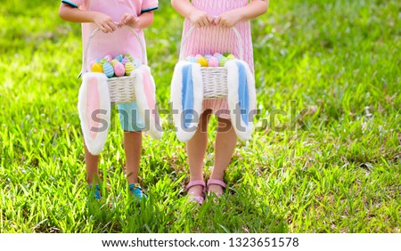 Kids with eggs basket and bunny ears on Easter egg hunt in sunny spring garden. Little boy and girl searching for colorful candy and chocolate eggs with rabbit basket. Children celebrating Easter.