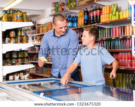 Happy glad friendly positive  family of father and teen son buying food products on shopping list in supermarket