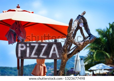 Big letters Pizza on wooden desk, beach, blue sky, red umbrella 