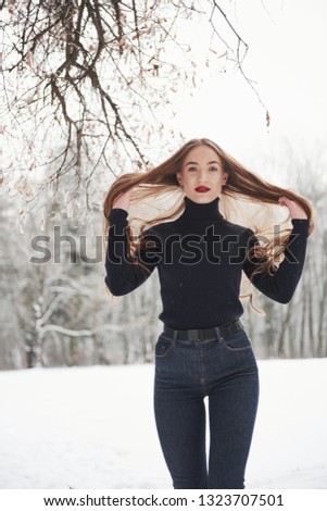 Decided to have a walk at weekend. Pretty girl with long hair and in black blouse is in the winter forest.