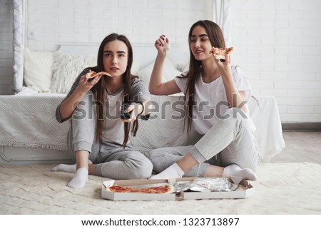 Girl searching something interesting. Sisters eating pizza when watching TV while sits on the floor of beautiful bedroom at daytime.