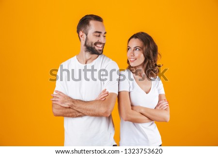 Portrait of pleased people man and woman in basic clothing smiling while standing together isolated over yellow background