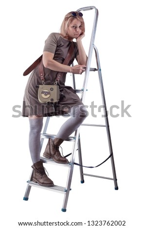 Young woman in dress and with retro movie camera posing on stepladder isolated on white background.