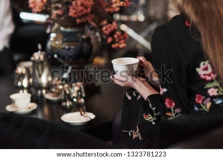Close up photo of girl sitting in the modern restaurant and holds white cup with tea.