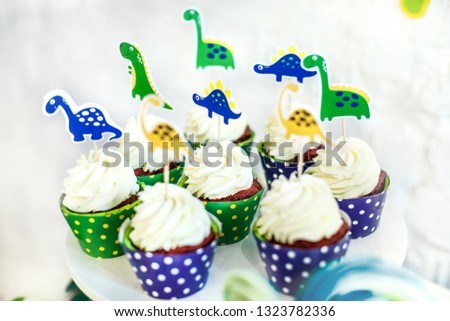 
Cupcakes on a plate with the image of dinosaurs. Festive table with sweets and cakes with cheese cream
