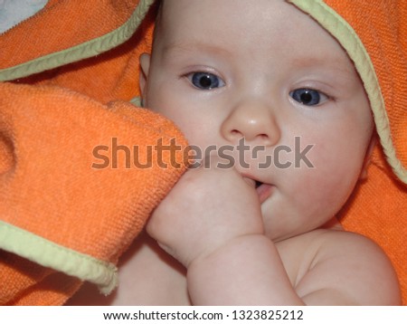 Little baby girl baby playing with an orange towel. After bathing, the baby is wrapped in a terry towel to keep warm.