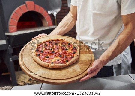 Strong man's hands. Picture of prepared delicious pizza with sausage rings and olives.