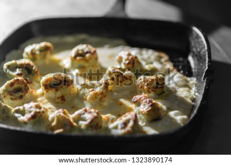 Homemade capeletti pasta with bechamel sauce in an black iron pan. Angle view. Italian cuisine