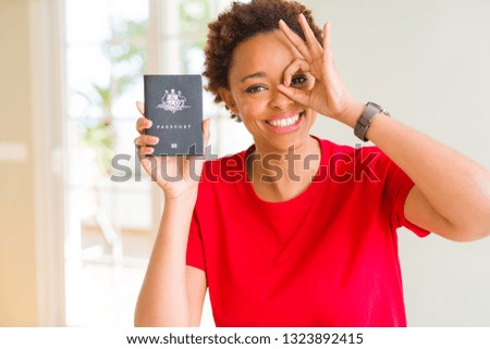 Young african american woman holding Australian passport with happy face smiling doing ok sign with hand on eye looking through fingers
