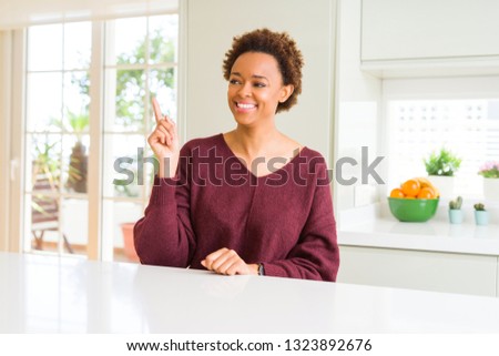 Young beautiful african american woman at home with a big smile on face, pointing with hand and finger to the side looking at the camera.