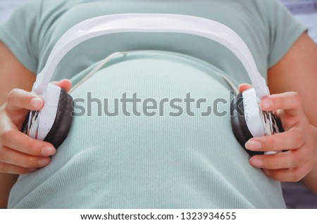 Pregnant woman Put headphones, turn the music on belly on a white background. Pregnancy, maternity, preparation and expectation concept. Beautiful tender mood photo of pregnancy.