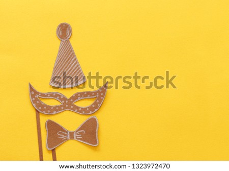 carnival party celebration concept with paper mask and clown hat over yellow background. Top view. Flat lay