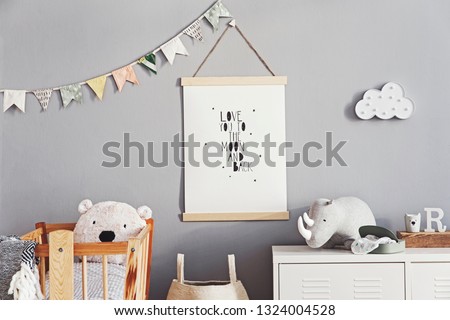 Stylish and cute scandinavian decor of  newborn baby room with mock up poster, natural toys, hanging decor flags and cloud, wooden cradle, basket for accessories and teddy bears. Grey walls .