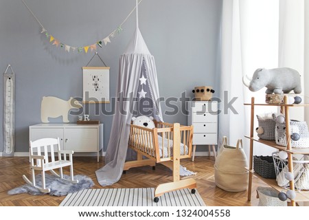 Stylish and bright scandinavian decor of  newborn baby room with mock up poster, white design furnitures, natural toys, hanging grey canopy with wooden cradle, bookstand, accessories and teddy bears. 