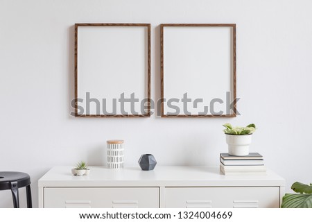 Minimalistic home decor of interior with two brown wooden mock up photo frames on the white shelf with books, beautiful plant in stylish pot, box and home accessories. White walls. Mockup concept.