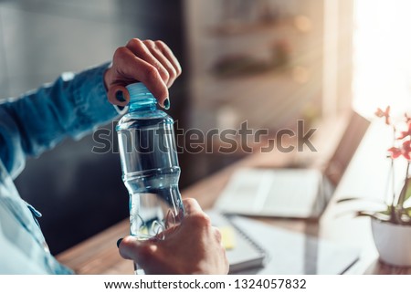 Woman wearing denim shirt working in the office and opening plastic bottle of water Royalty-Free Stock Photo #1324057832