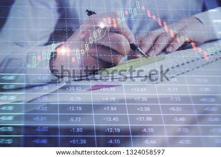Close up of hands writing with double exposure of business charts. Financial concept.